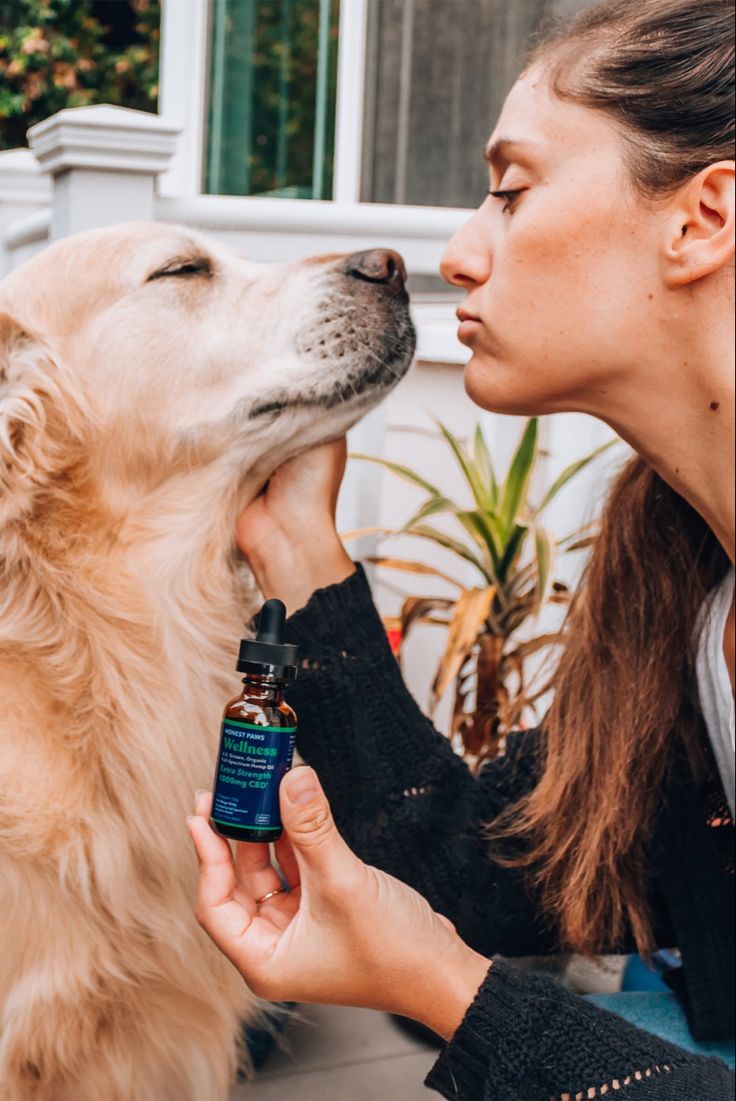 Woman gently holding a calming oil bottle while comforting her dog, showcasing dog anxiety relief products.